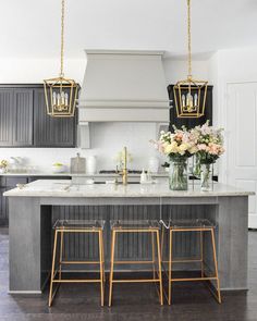 a kitchen island with three stools in front of it and flowers on the counter