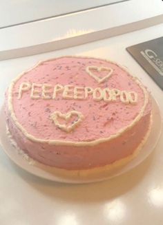 a pink cake with the word peepopo on it sitting next to a book