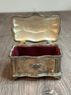 an ornate silver box with a red velvet lining on the inside sits on a wooden surface