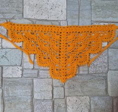 an orange crocheted triangle is hanging on a brick wall next to a stone floor