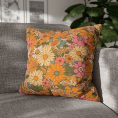 an orange and pink flowered pillow sitting on top of a gray couch next to a potted plant