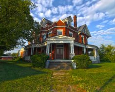 an old victorian style house in the middle of a grassy area with trees and bushes