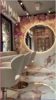 the interior of a salon with white chairs and flowers on the wall behind the mirror