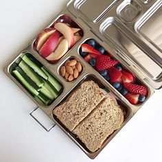 an open lunch box with fruits, vegetables and crackers on the side is shown