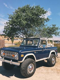 an old blue truck parked in front of a tree