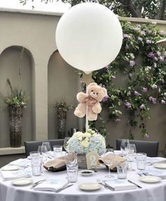 a teddy bear sitting on top of a table next to a white balloon with the number twenty