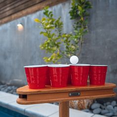 four red cups sitting on top of a wooden table next to a pool with a ping pong ball in it