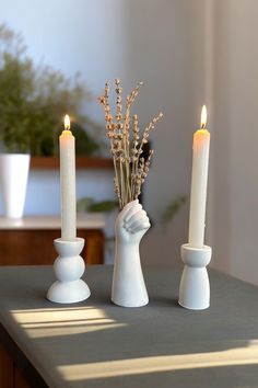 three white candles sitting on top of a table next to vases with flowers in them