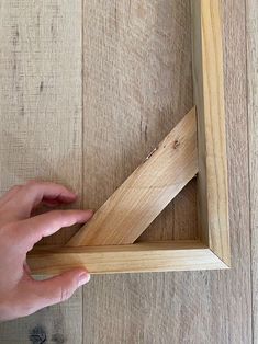 a person holding a piece of wood in front of a frame on a wooden floor