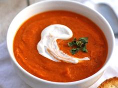 a bowl of tomato soup with sour cream on top and a piece of bread next to it