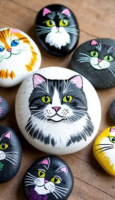 painted rocks with cats on them sitting on a wooden table next to each other and looking up at the camera