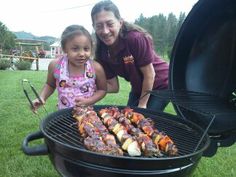 a woman and girl standing next to a bbq grill