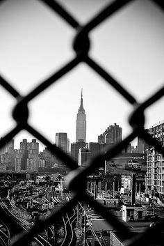 black and white photograph of the empire state building through a chain link fence