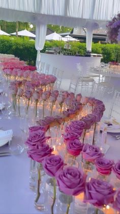 the table is set up with pink roses and candles in clear vases on each side