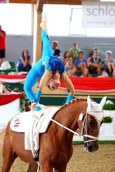 a woman is doing a handstand on top of a horse while people watch