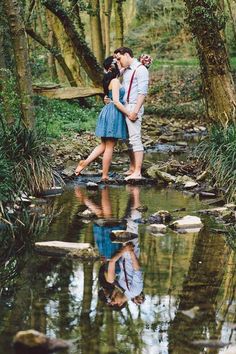 a man and woman are kissing in the middle of a stream with trees around them