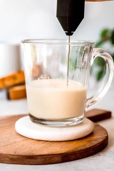 a person pouring milk into a glass cup on top of a wooden cutting board,