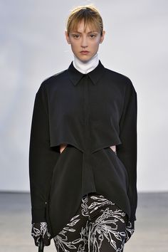 a model walks down the runway in a black coat with white flowers on it,