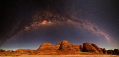 the milky shines brightly in the night sky over some rocks and desert terrain,