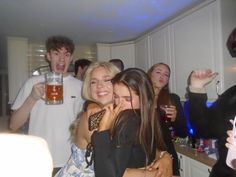 a group of people standing in a kitchen next to each other holding drinks and talking on cell phones