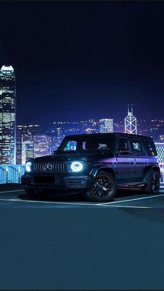 a black jeep parked in front of a cityscape at night with the lights on