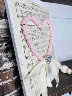 a pink heart shaped beaded bracelet sitting on top of a wooden bench next to sheet music