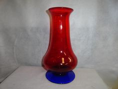 a red glass vase sitting on top of a blue base in front of a white background