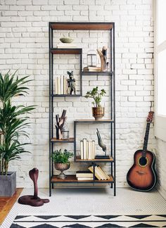 a guitar and bookshelf in front of a brick wall with plants on it