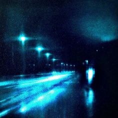 blurry photograph of street lights at night in the rain with no one on it