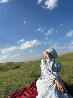 a woman sitting on top of a red blanket in the middle of a green field