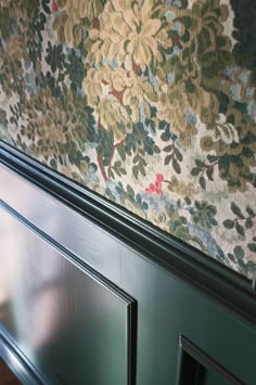 a close up of a metal door with floral wall paper on the walls behind it