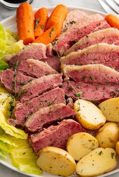 a white plate topped with meat, potatoes and carrots next to lettuce