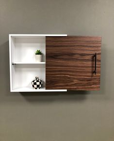 a wall mounted shelf with two shelves and a vase on the bottom, in front of a gray wall