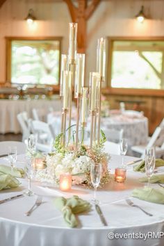 the centerpieces on this table are tall, slender candles with flowers and greenery