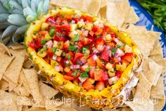 a pineapple with fruit and salsa in it surrounded by chips