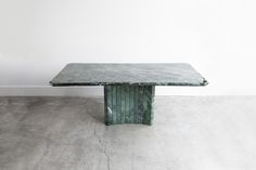 a green marble table sitting on top of a cement floor next to a white wall