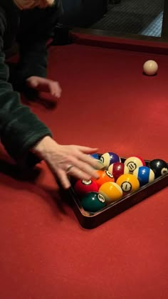 a person reaching for a pool ball in a pool table with several balls on it