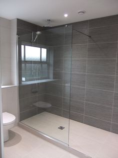 a white toilet sitting next to a shower in a bathroom with gray tile on the walls