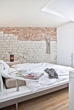 a white bed sitting in a bedroom next to a brick wall on top of a hard wood floor