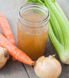 carrots, celery and onion sit on a table next to a jar of liquid