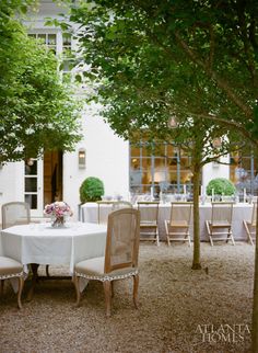 an outdoor dining area with white table cloths and wooden chairs, surrounded by trees