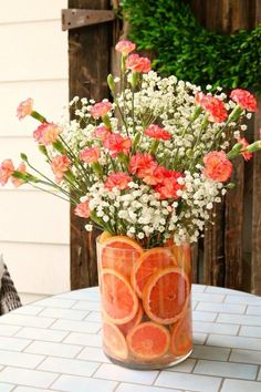 a vase filled with orange slices and flowers on top of a white tiled table next to a wooden fence