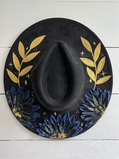 a black hat with blue and yellow flowers on it hanging from the side of a white wall