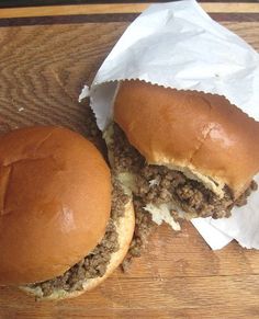 two hamburgers sitting next to each other on top of a wooden cutting board with wax paper