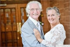 an older man and woman are posing for a photo in front of the door to their wedding venue