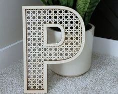 the letter p is placed next to a potted plant on the carpeted floor