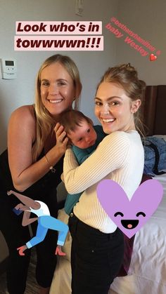 two women holding a baby in their arms and smiling at the camera with an i love you sign above them