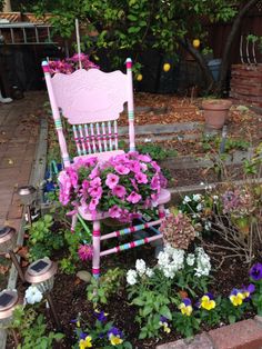 a pink rocking chair with flowers growing in it and some potted plants on the ground