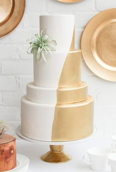 a white and gold wedding cake with succulents on top, surrounded by plates