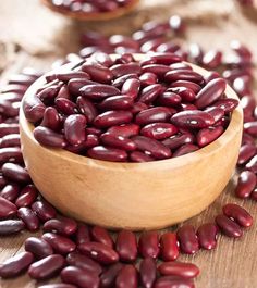 a wooden bowl filled with red beans on top of a table